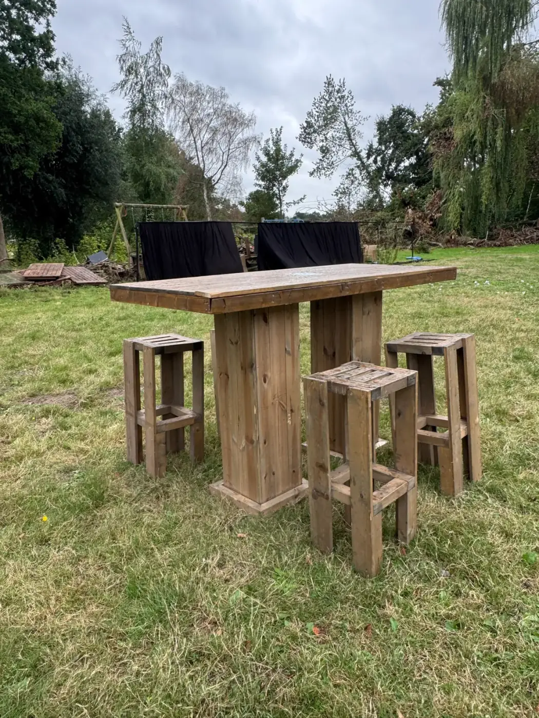 Houten statafel met bijpassende houten krukken op het gras, een stoere keuze om meubilair te huren voor een receptie in Duffel