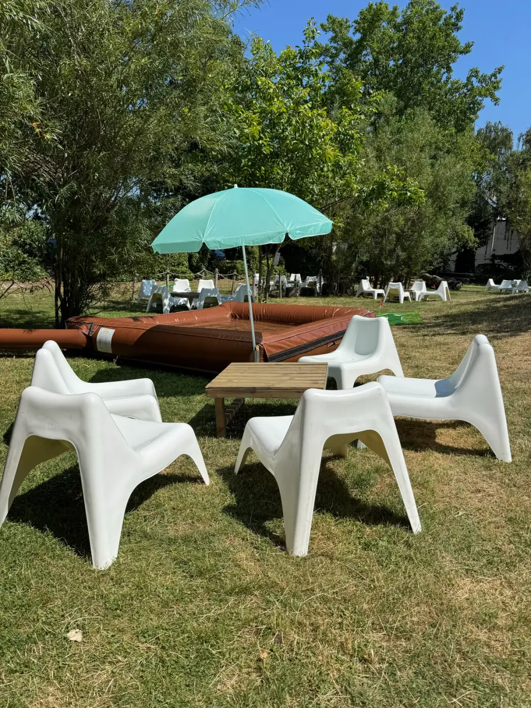 Witte loungestoelen rond een houten tafeltje met een mintgroene parasol in de tuin, aangenaam om meubilair te huren voor een zomerreceptie in Beveren