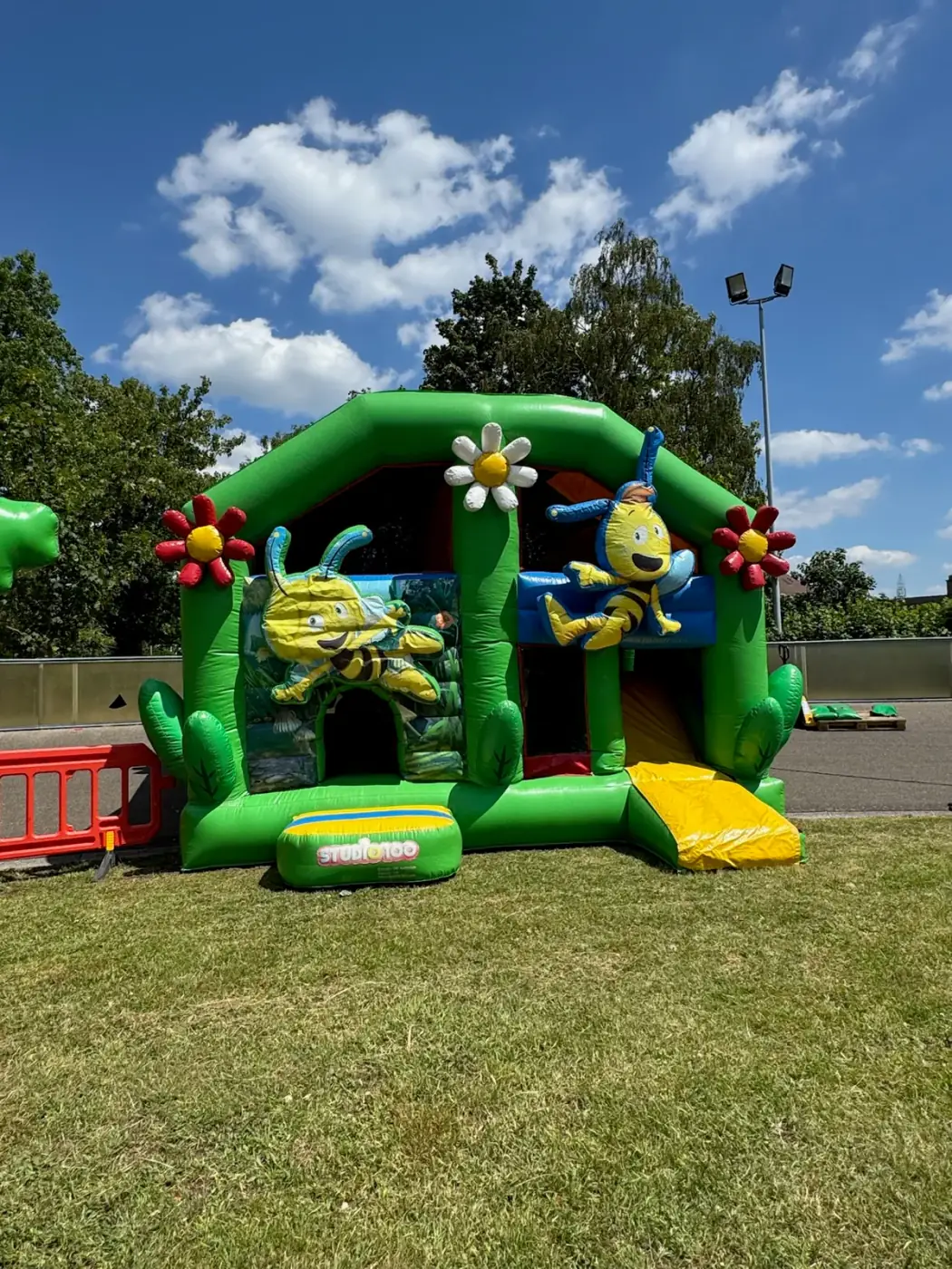 Groen springkasteel met bijen en bloemen op een zonnig grasveld, klaar om een springkasteel te huren voor een kinderfeest in Boom