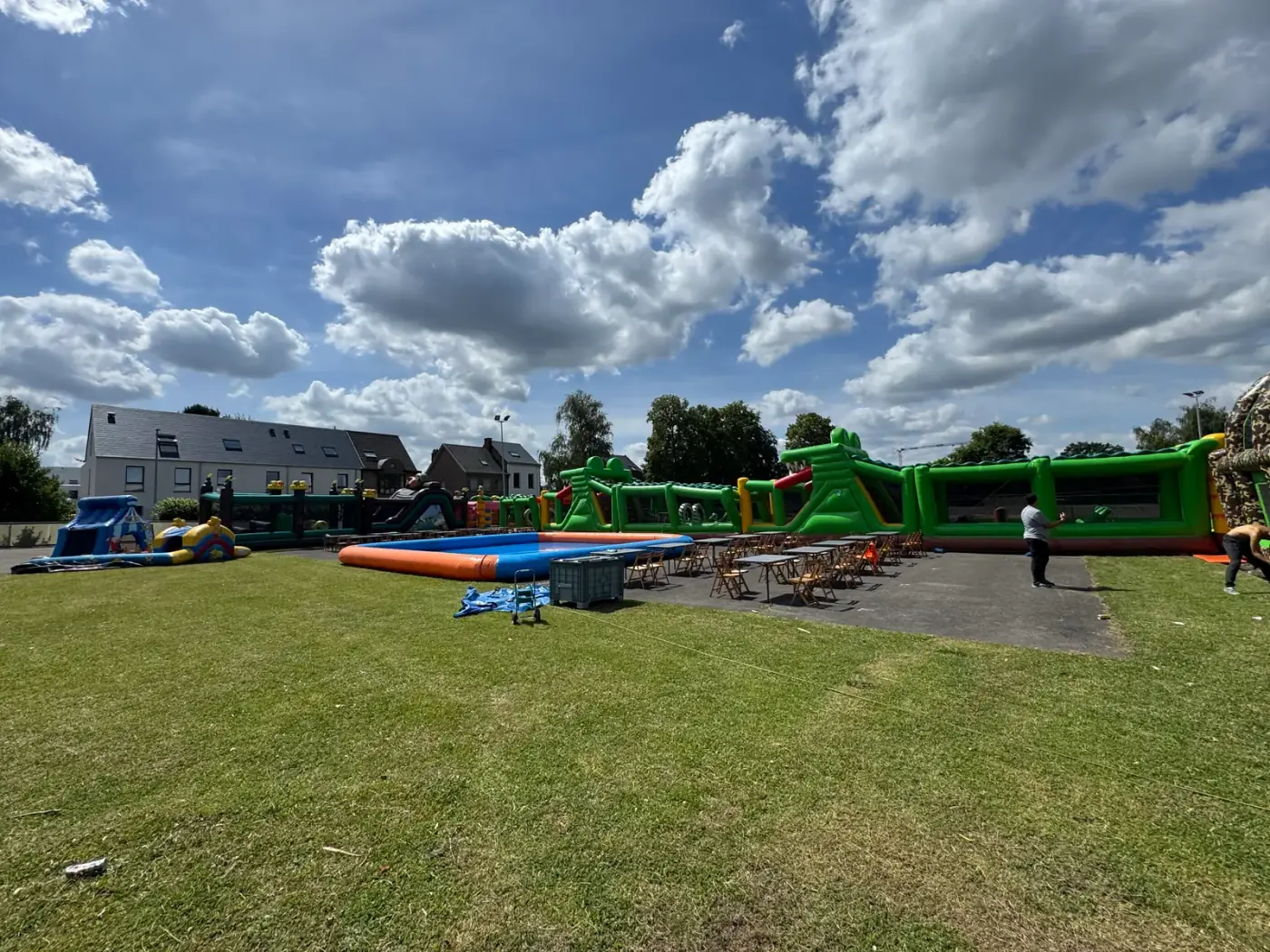 Lange opblaasbare stormbaan naast een opblaasbaar zwembad op een groot grasveld, een uitdagend alternatief wanneer je een springkasteel wil huren voor een buurtfeest in Ranst