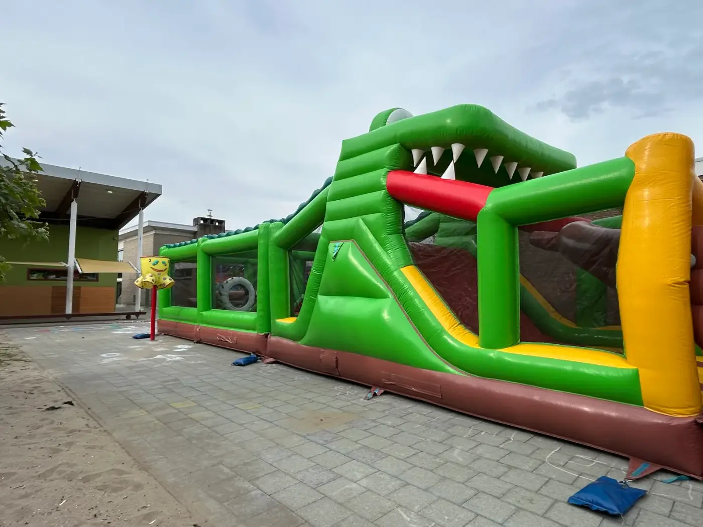 Groene opblaasbare stormbaan met een krokodillenkop aan de ingang op een speelplaats, een stoer alternatief wanneer je een springkasteel wil huren voor een schoolfeest in Mechelen