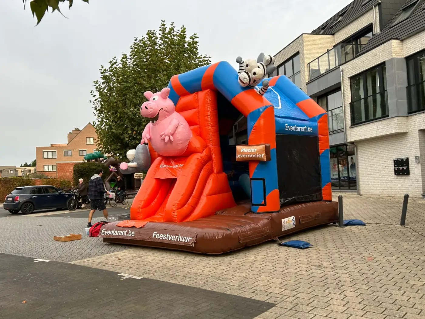 Oranje met blauw springkasteel met boerderijdieren opgesteld op straat in een woonwijk, een vlotte keuze om een springkasteel te huren voor een straatfeest in Schelle