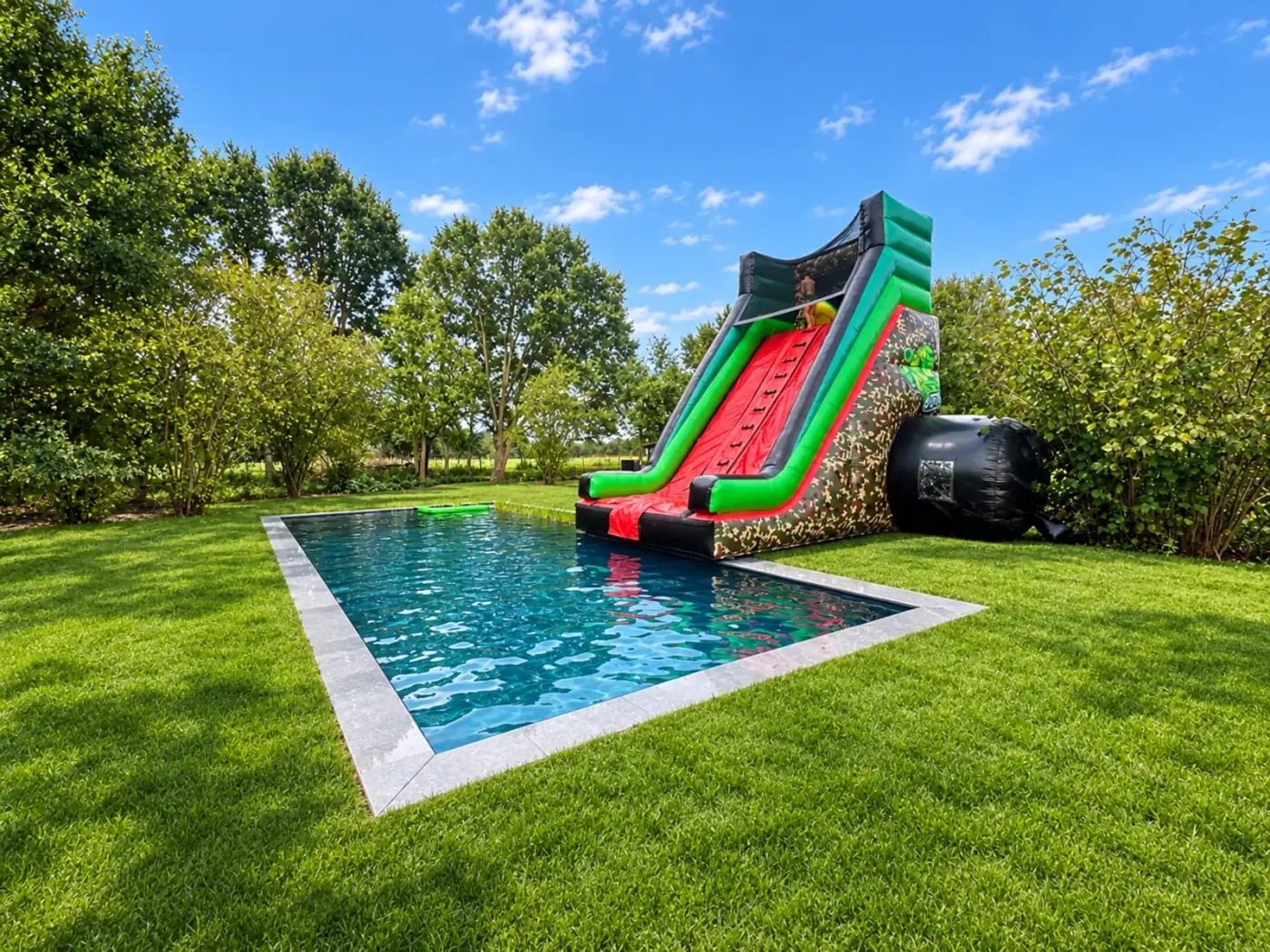 Opblaasbare waterglijbaan die uitkomt in een zwembad in een zonnige tuin, een populaire keuze om een springkasteel te huren voor een zomerfeest in Hemiksem
