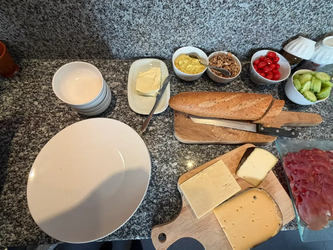 Bovenaanzicht van een buffet met borden, kommetjes, kaasplanken en een broodmes, een volledig servies om tafelgerei te huren voor een receptie in Schilde