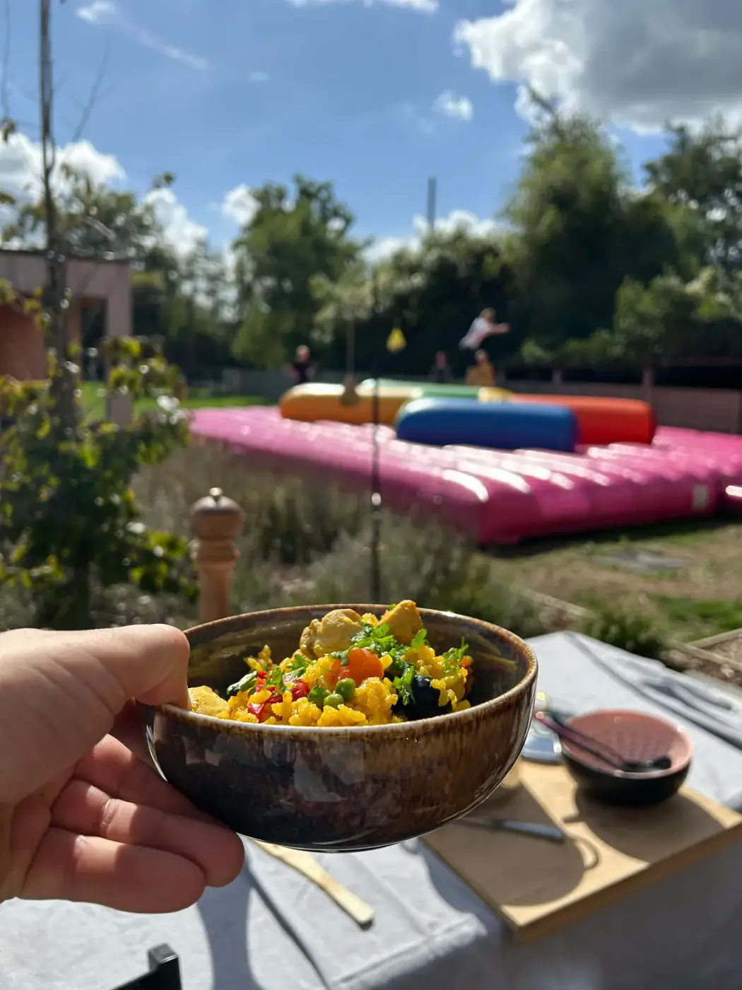 Kom met paella boven een gedekte tafel met bestek en een springkussen op de achtergrond, praktisch om tafelgerei te huren voor een tuinfeest in Deurne