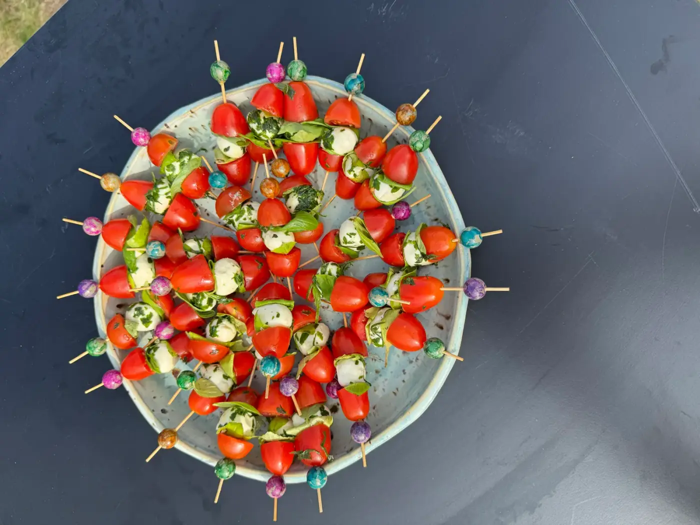 Ronde serveerschaal met tomaat-mozzarellaspiesjes op een zwarte statafel, perfect om tafelgerei te huren voor een walking dinner in Hemiksem