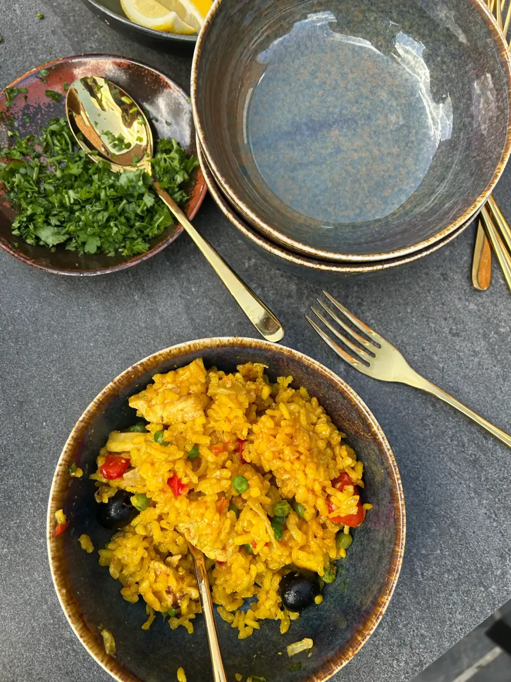 Keramische kom met paella, extra borden en goudkleurig bestek van bovenaf gefotografeerd, stijlvol om tafelgerei te huren voor een diner in Kontich