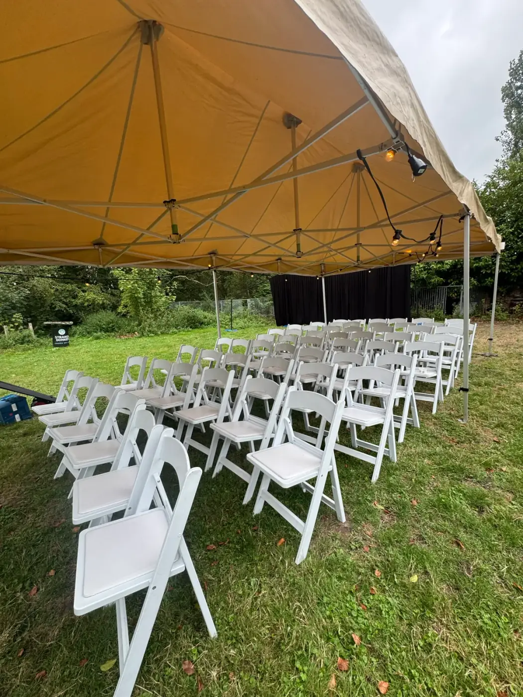 Rijen witte klapstoelen op het gras onder een beige vouwtent met lichtslinger, de klassieke opstelling om een tent te huren voor een ceremonie in Brasschaat