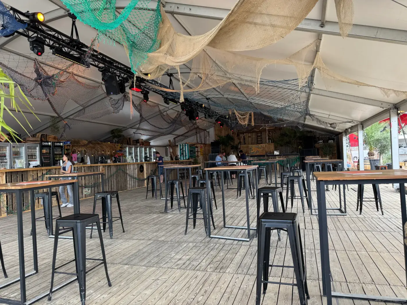 Binnenkant van een grote feesttent met zwarte statafels, barkrukken en een houten toog, geschikt om een tent te huren voor een evenement in Duffel