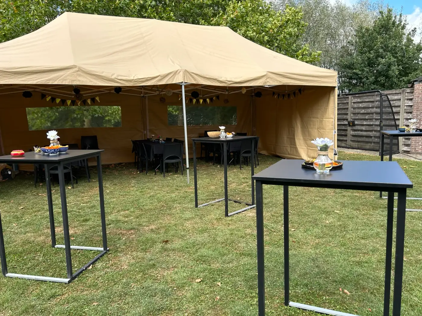Beige vouwtent met zwarte statafels op het gazon, een strakke opstelling om een tent te huren voor een receptie in Rumst