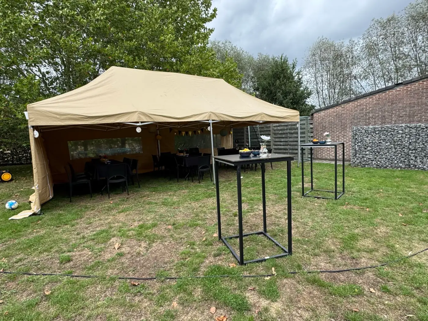 Beige vouwtent met zijwanden en statafels ervoor op een grasveld, een praktische oplossing om een tent te huren voor een tuinfeest in Lint